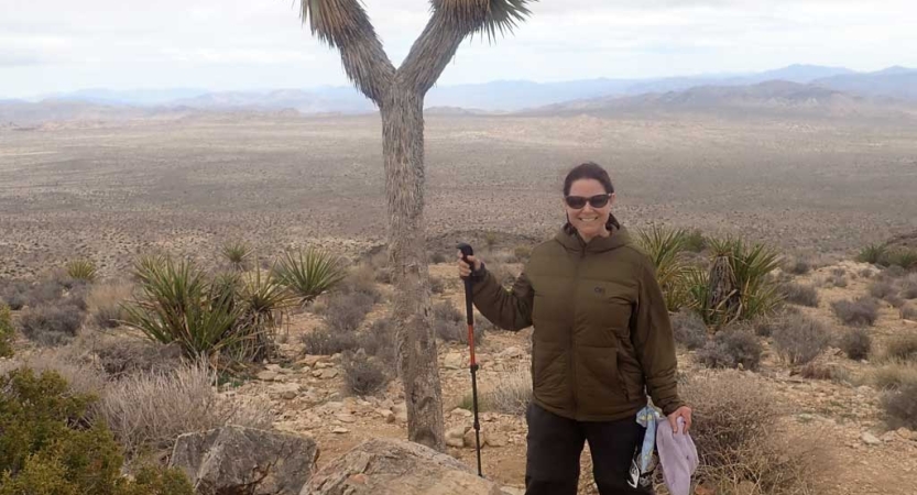 A person smiles while standing in a vast desert landscape